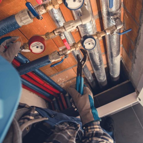 Aerial View of Plumber with Hydraulic Key Performing Hot and Cold Water Meters Service and Repair. Residential Water Supply Theme.