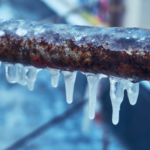 Many small icicles have frozen on a rusty pipe in the street in the winter