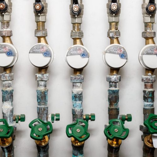 Lot of cool water consumption meters for each apartment on pipeline system in residential building. Dirty plumbing pipes with water meters and faucets in the basement of the house