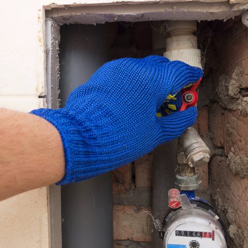 The plumber in safety blue gloves closes or opens the water valve at home.